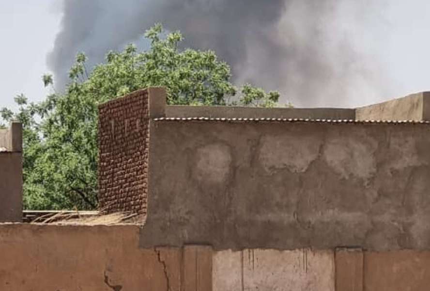 Kind steht vor einem Haus im Sudan nach Ausbruch des Krieges, es steigt Rauch auf.